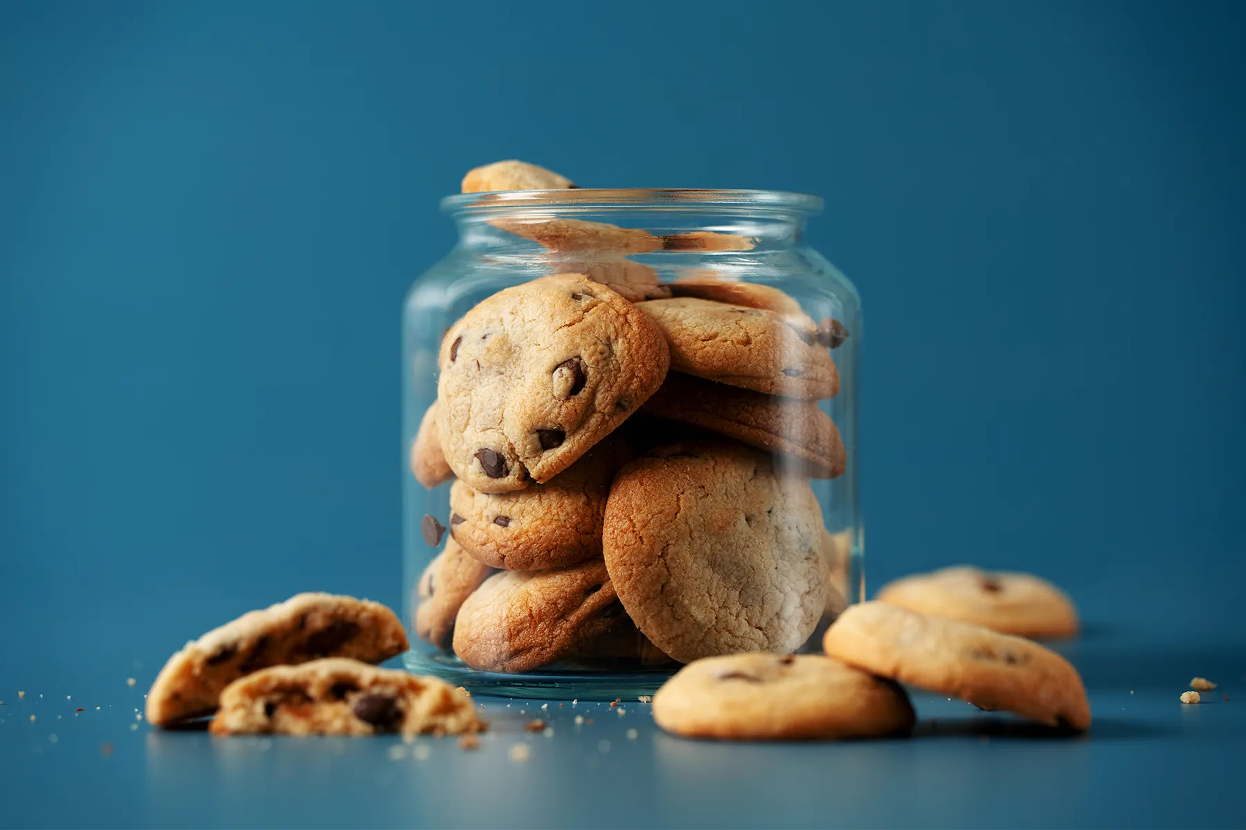 Biscoitos de chocolate em pote de vidro sobre fundo azul, perfeitos para um lanche saboroso.