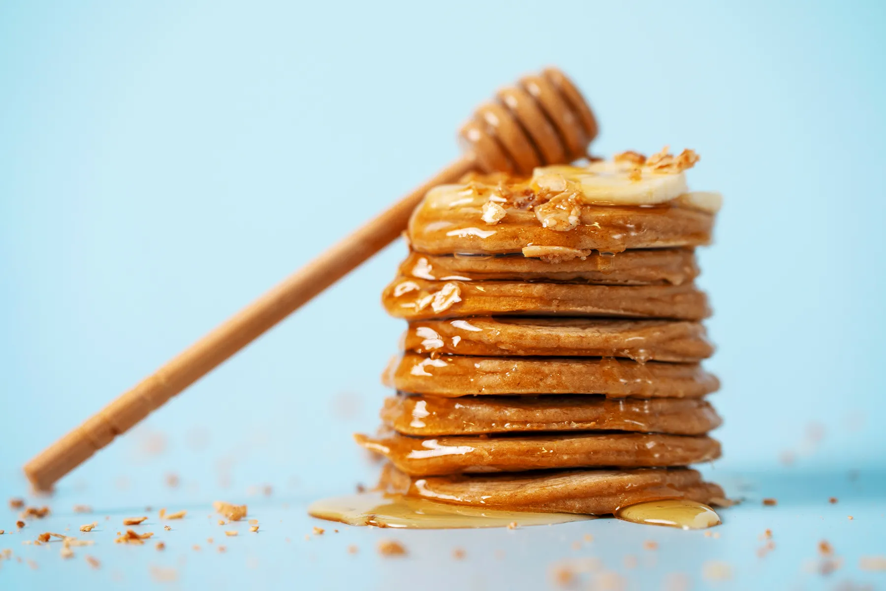 Pilha de panquecas com mel e aveia em fundo azul claro. Receita de café da manhã saudável e deliciosa.