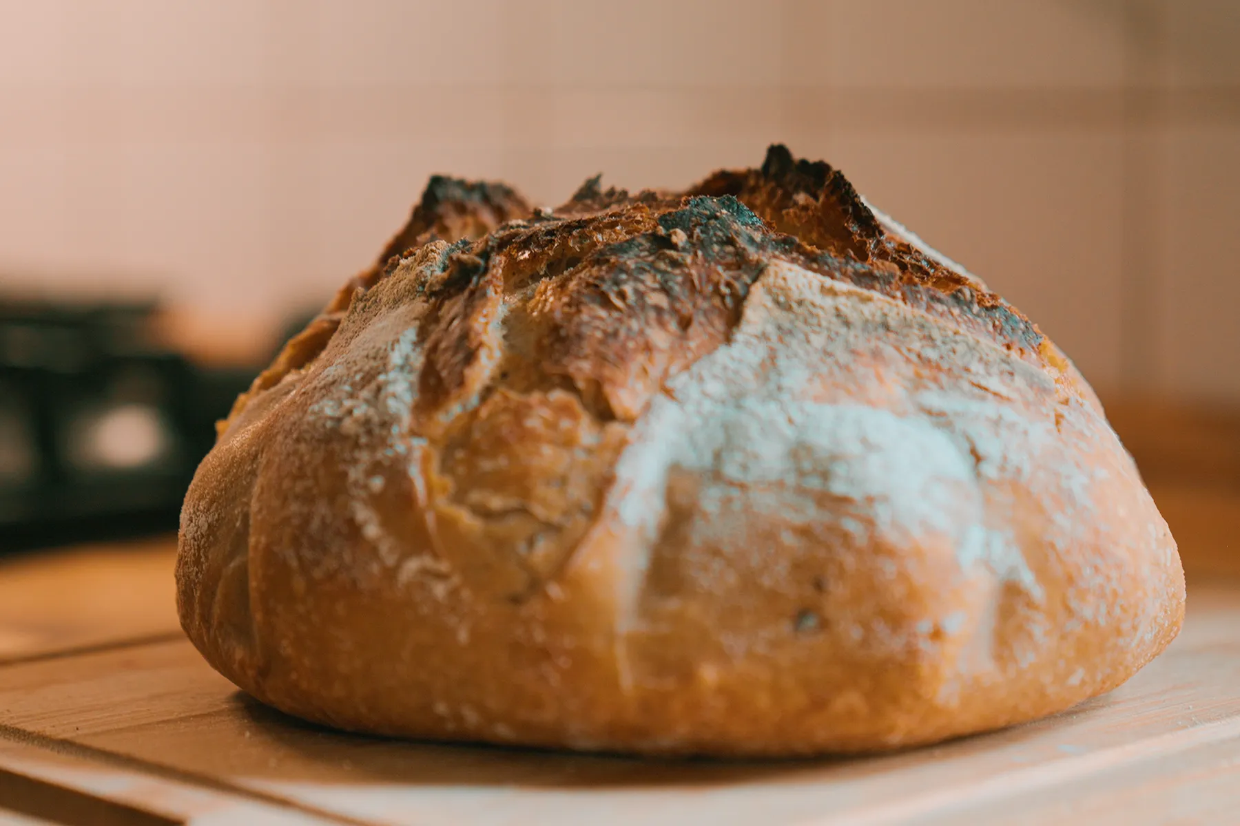 Pão artesanal recém-assado sobre tábua de madeira na cozinha, com crosta dourada e textura rústica.